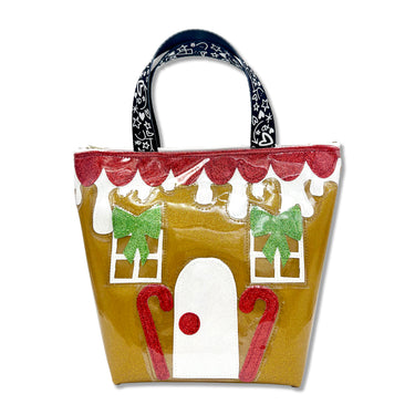 Super cute gingerbread handle bag featuring vibrant green, white, and red glitter canvas details, this charming gingerbread house sparkles on a rich gingerbread-gold glitter vinyl bag. Finished with Julie Mollo! doodle-printed handles, this unique accessory is the perfect signature winter holiday statement piece. Bag is pictured on a white background.