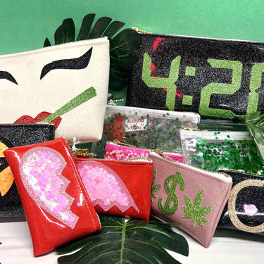 collection of kush kard x Julie Mollo clutches, makeup bags, and cosmetic bags with leaf props against a green background.